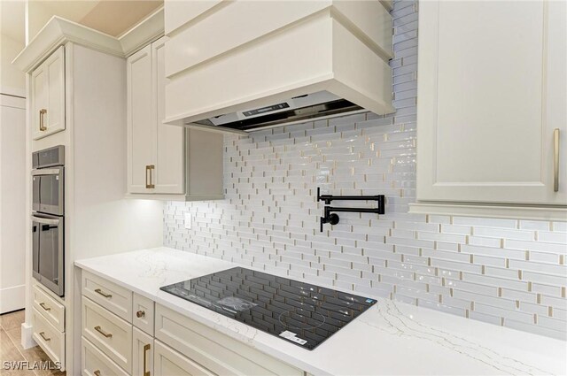 6100 Riverside Dr, Punta Gorda, FL 33982 - kitchen with premium range hood, black electric stovetop, decorative backsplash, light stone counters, and stainless steel double oven