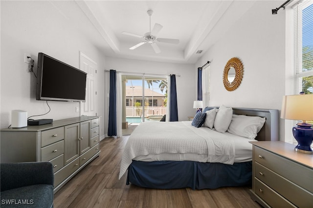 bedroom with a raised ceiling, multiple windows, access to exterior, and wood finished floors