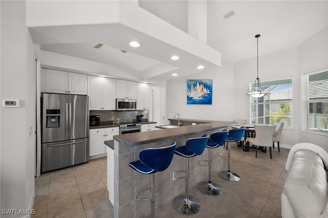 kitchen featuring appliances with stainless steel finishes, dark countertops, light tile patterned flooring, a kitchen breakfast bar, and white cabinetry