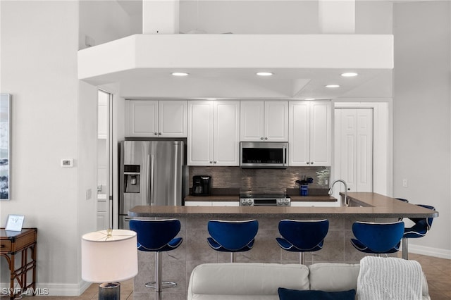 kitchen with appliances with stainless steel finishes, a breakfast bar area, dark countertops, baseboards, and white cabinetry
