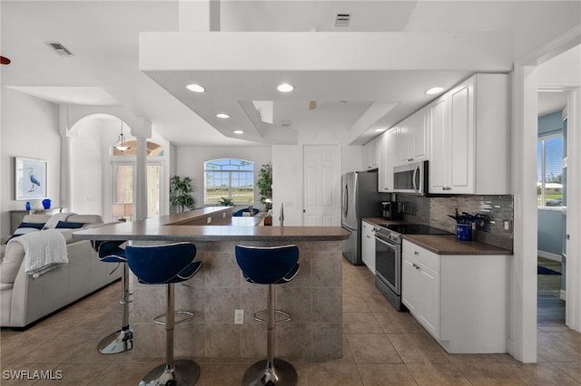 kitchen with stainless steel appliances, dark countertops, ornate columns, a kitchen breakfast bar, and open floor plan