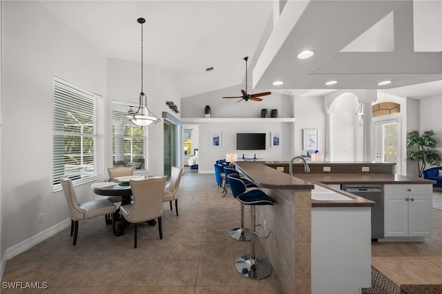 kitchen with dishwasher, a sink, dark countertops, open floor plan, and light tile patterned floors