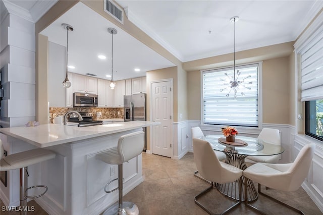 9469 Casoria Ct Unit 101, Naples, FL 34113 - kitchen featuring appliances with stainless steel finishes, a peninsula, wainscoting, a breakfast bar, and light countertops
