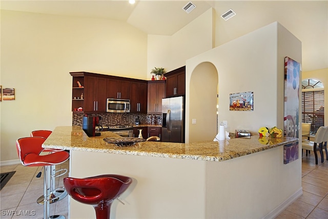 kitchen with stainless steel appliances, light tile patterned floors, arched walkways, light stone countertops, and high vaulted ceiling