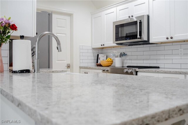1300 Hilltop Dr, Naples, FL 34103 - kitchen with stainless steel microwave, white cabinetry, decorative backsplash, and light stone counters