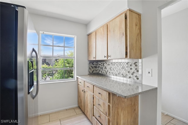 kitchen with stainless steel refrigerator with ice dispenser, tasteful backsplash, baseboards, and light brown cabinetry
