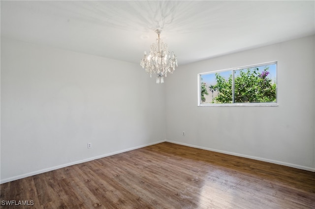 unfurnished room featuring a chandelier, wood finished floors, and baseboards