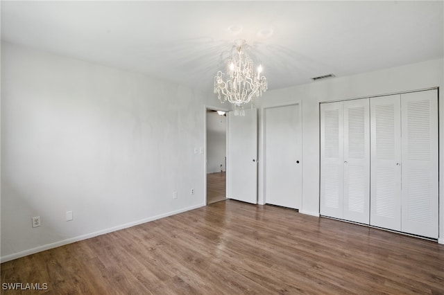 unfurnished bedroom with a chandelier, wood finished floors, two closets, and baseboards