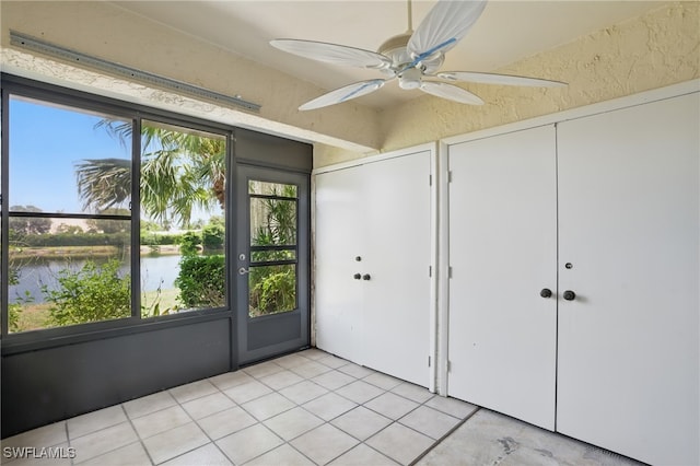 unfurnished bedroom with a water view, light tile patterned flooring, and ceiling fan