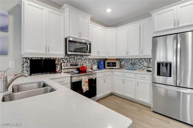 1256 Enbrook Loop, Naples, FL 34114 - kitchen featuring stainless steel appliances, a sink, white cabinets, tasteful backsplash, and light wood finished floors