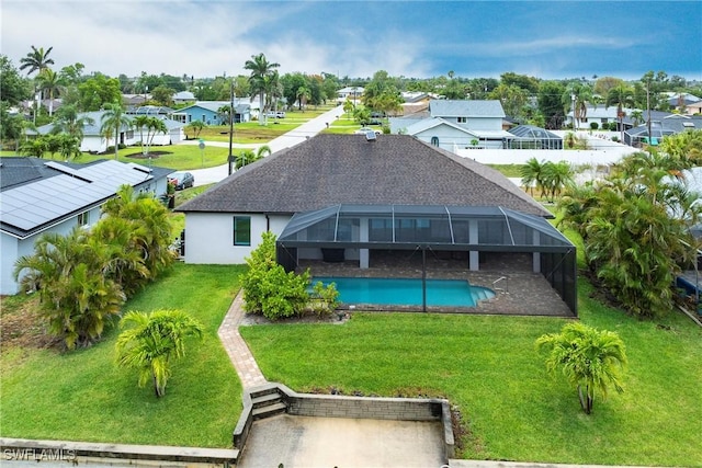 rear view of property featuring a residential view, a yard, an outdoor pool, and glass enclosure