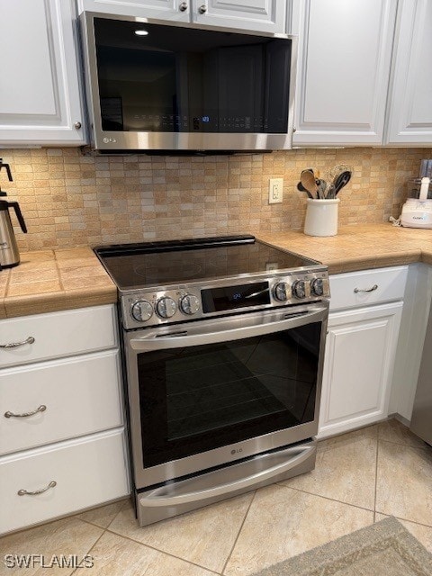 2880 Gulf Shore Blvd N Unit 404, Naples, FL 34103 - kitchen with appliances with stainless steel finishes, light tile patterned flooring, white cabinets, and decorative backsplash