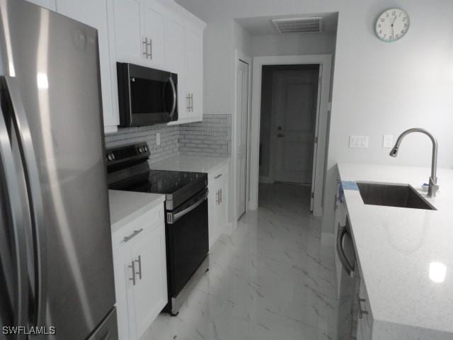 3805 6th St W, Lehigh Acres, FL 33971 - kitchen with appliances with stainless steel finishes, a sink, white cabinets, backsplash, and light marble finish floors