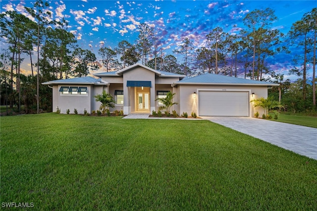 prairie-style home with stucco siding, a garage, a front yard, driveway, and metal roof