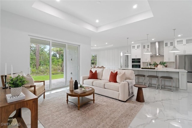 living area featuring recessed lighting, light marble finish floors, and a tray ceiling
