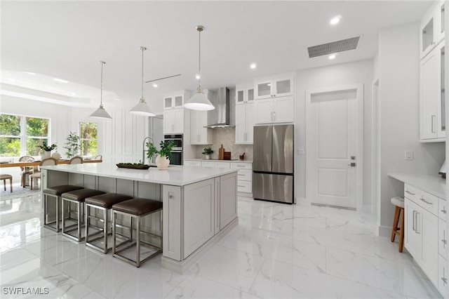 kitchen featuring appliances with stainless steel finishes, wall chimney range hood, a kitchen bar, decorative backsplash, and recessed lighting