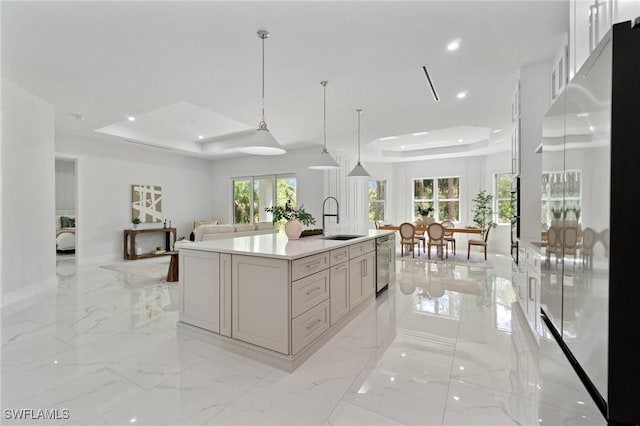 kitchen featuring a raised ceiling, stainless steel appliances, a sink, open floor plan, and light marble finish floors