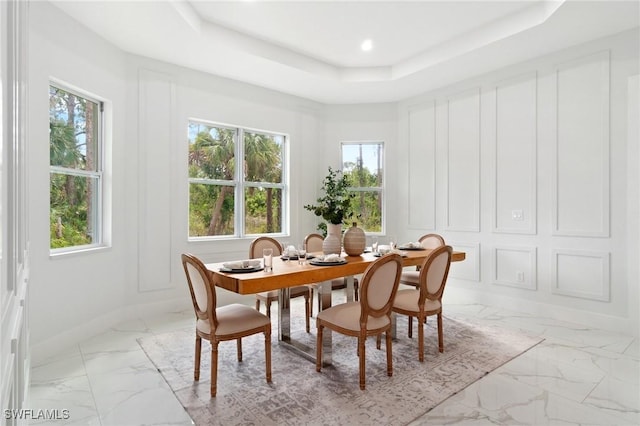 dining space featuring light marble finish floors, a tray ceiling, and baseboards
