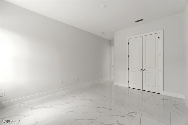 unfurnished bedroom featuring marble finish flooring, baseboards, and a closet