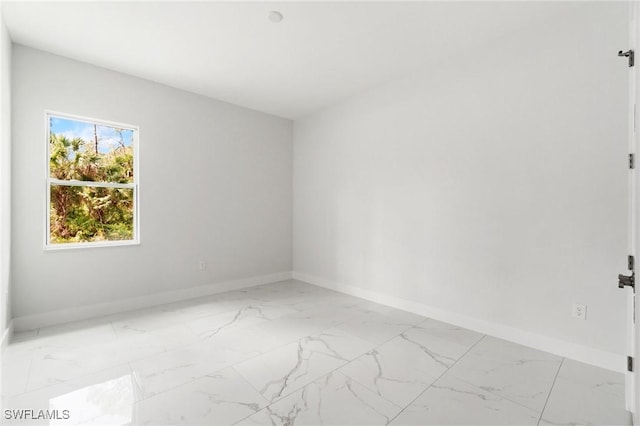 unfurnished room featuring light marble finish flooring and baseboards