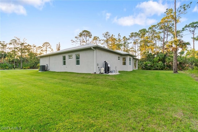 rear view of house featuring stucco siding, central AC unit, and a lawn