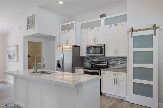 8970 Woodgate Manor Ct, Fort Myers, FL 33908 - kitchen featuring appliances with stainless steel finishes, a sink, light wood finished floors, decorative backsplash, and a center island with sink
