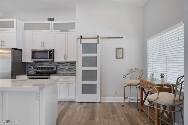 8970 Woodgate Manor Ct, Fort Myers, FL 33908 - kitchen with appliances with stainless steel finishes, wood finished floors, decorative backsplash, white cabinetry, and a barn door