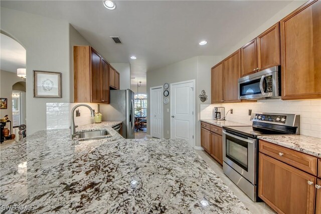 16112 Cutters Ct, Fort Myers, FL 33908 - kitchen featuring appliances with stainless steel finishes, a sink, arched walkways, light stone countertops, and backsplash
