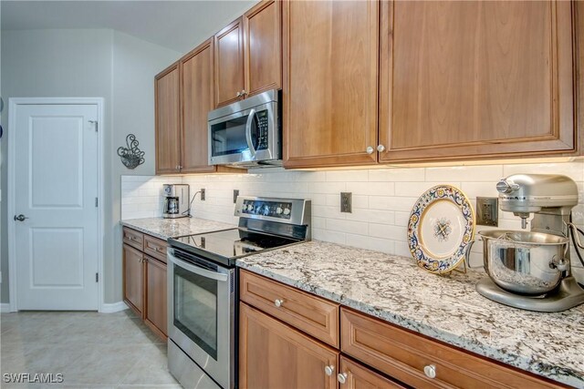 16112 Cutters Ct, Fort Myers, FL 33908 - kitchen featuring stainless steel appliances, light stone counters, tasteful backsplash, brown cabinets, and light tile patterned floors