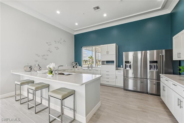 16811 Elkhorn Coral Dr, North Fort Myers, FL 33903 - kitchen with high end refrigerator, a breakfast bar, a peninsula, white cabinetry, and crown molding