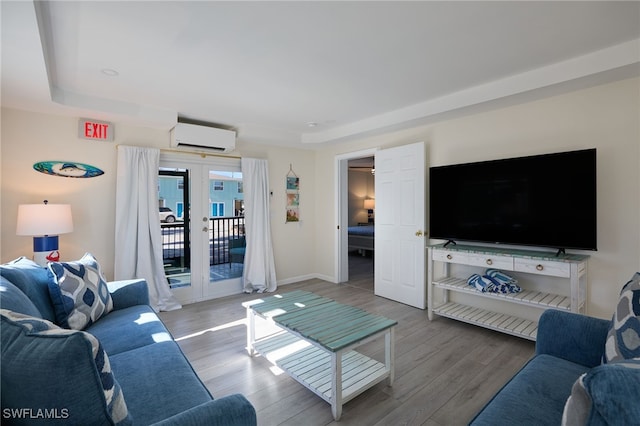 living area featuring a wall mounted AC, wood finished floors, baseboards, and a raised ceiling