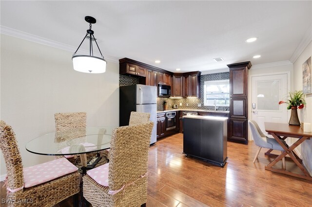 kitchen with appliances with stainless steel finishes, crown molding, a kitchen island, light wood-style flooring, and dark brown cabinetry
