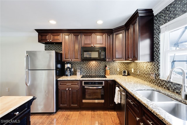 kitchen with black appliances, a sink, ornamental molding, decorative backsplash, and light wood-type flooring