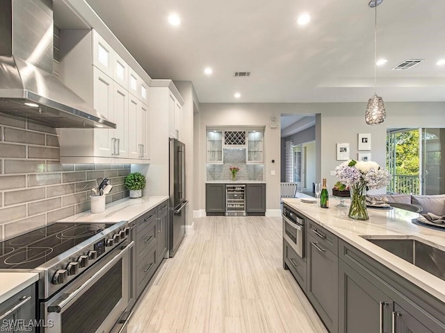 2452 Terra Verde Ln Unit 2452, Naples, FL 34105 - kitchen with high quality appliances, wall chimney exhaust hood, beverage cooler, white cabinets, and decorative backsplash