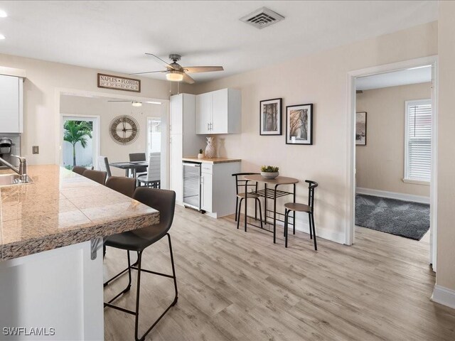 698 99th Ave N, Naples, FL 34108 - kitchen featuring a kitchen bar, tile counters, white cabinetry, light wood-style floors, and baseboards