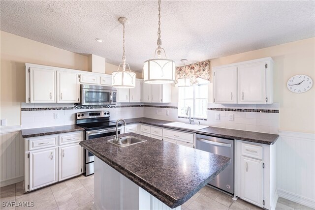 19703 Eagle Trace Ct, North Fort Myers, FL 33903 - kitchen featuring stainless steel appliances, white cabinetry, a wainscoted wall, an island with sink, and a textured ceiling