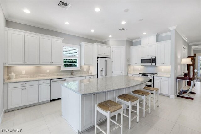 8396 Promoso Ct, Naples, FL 34114 - kitchen with white appliances, crown molding, a center island, white cabinetry, and a breakfast bar