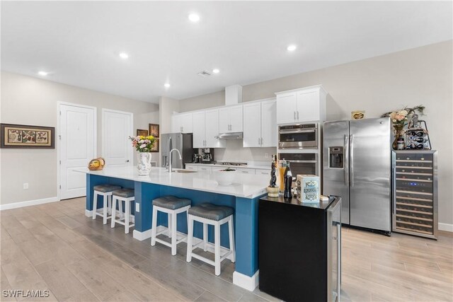 20467 Napa Loop, Estero, FL 33928 - kitchen with stainless steel appliances, wine cooler, a large island with sink, a kitchen bar, and white cabinetry