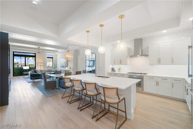 875 6th Ave S Unit 304, Naples, FL 34102 - kitchen with appliances with stainless steel finishes, wall chimney range hood, a sink, light wood finished floors, and a kitchen bar