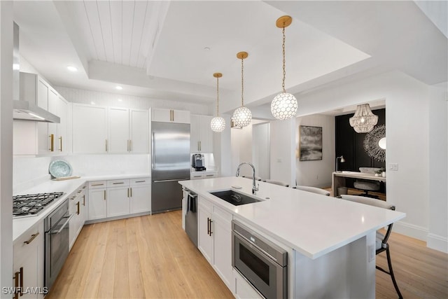 875 6th Ave S Unit 304, Naples, FL 34102 - kitchen with built in appliances, a sink, a tray ceiling, wall chimney exhaust hood, and light wood-type flooring