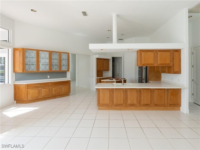 561 Conover Ct, Marco Island, FL 34145 - kitchen with a peninsula, light countertops, brown cabinets, glass insert cabinets, and a high ceiling