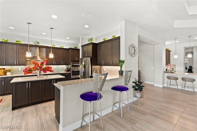 4382 Caldera Cir, Naples, FL 34119 - kitchen featuring appliances with stainless steel finishes, wall chimney range hood, a peninsula, dark brown cabinetry, and decorative backsplash