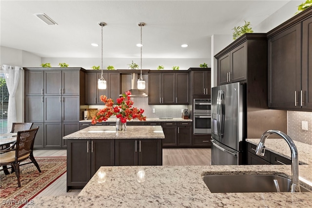 4382 Caldera Cir, Naples, FL 34119 - kitchen featuring stainless steel appliances, a sink, wall chimney exhaust hood, light wood-style floors, and dark brown cabinetry