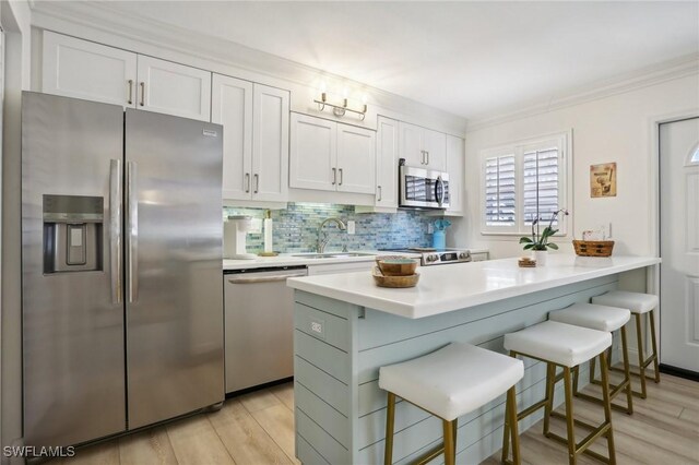 980 7th Ave S Unit 104, Naples, FL 34102 - kitchen featuring stainless steel appliances, a kitchen bar, light countertops, decorative backsplash, and light wood-type flooring