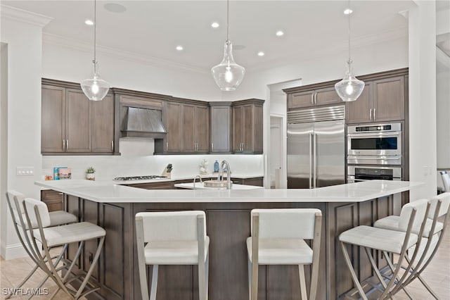4249 Deephaven Ln, Naples, FL 34119 - kitchen featuring appliances with stainless steel finishes, premium range hood, crown molding, light countertops, and a large island with sink