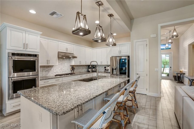 9292 Cayman Dr, Naples, FL 34114 - kitchen with appliances with stainless steel finishes, a sink, under cabinet range hood, decorative backsplash, and white cabinetry