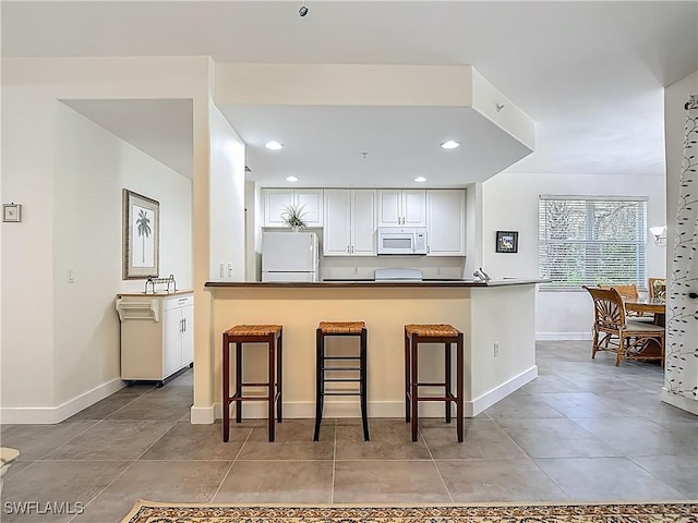 1732 Tarpon Bay Dr S Unit 101, Naples, FL 34119 - kitchen featuring white appliances, dark countertops, white cabinets, a kitchen breakfast bar, and recessed lighting
