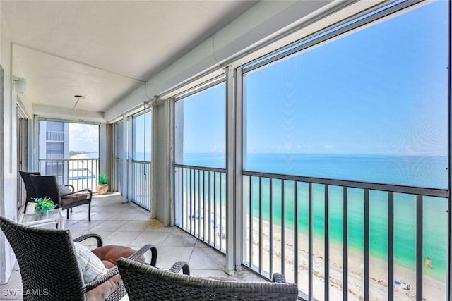 sunroom / solarium featuring view of water and beach and tile patterned floors