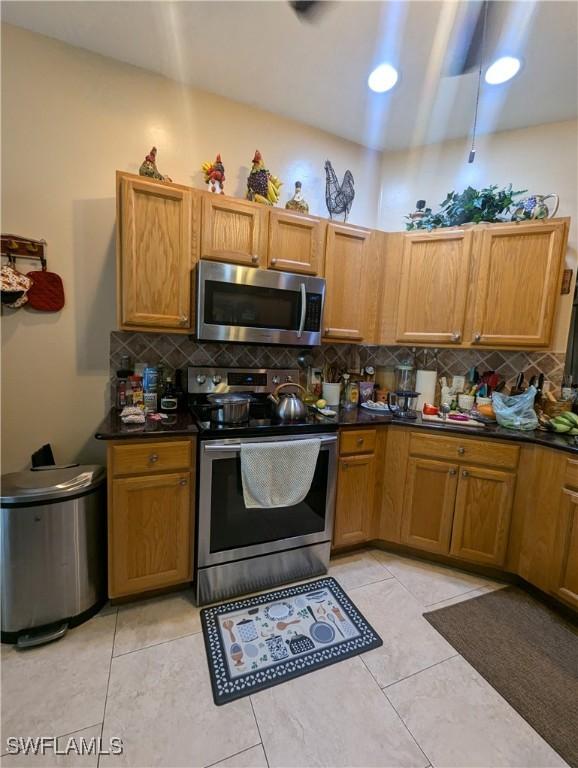 1711 NW 28th Ter, Cape Coral, FL 33993 - kitchen featuring stainless steel appliances, backsplash, dark countertops, and brown cabinetry
