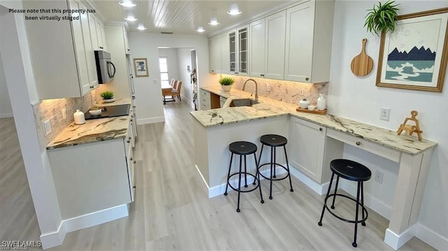 718 Reef Point Cir, Naples, FL 34108 - kitchen featuring stainless steel microwave, a breakfast bar area, light wood-style floors, and glass insert cabinets